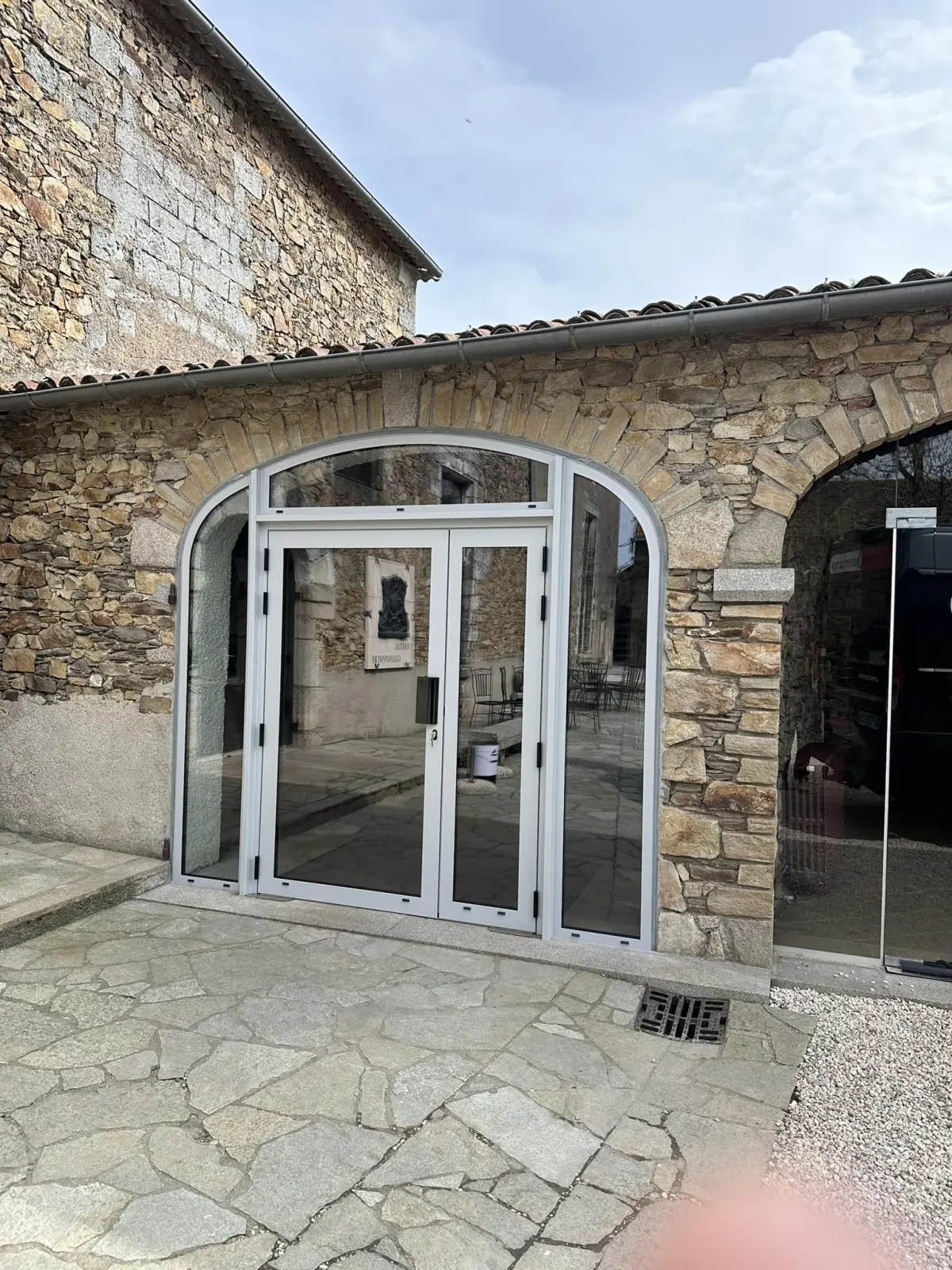 Double porte vitrée aluminium blanc cintrée sur façade pierre